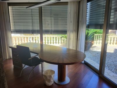 Bureau privé spacieux avec un grand bureau en bois et parquet. Les baies vitrées donnent sur une balustrade et un jardin méditerranéen.