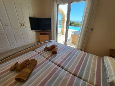 Chambre avec deux lits simples, une armoire intégrée et une télévision murale. Accès direct à la piscine extérieure avec une arche et des vues dégagées.