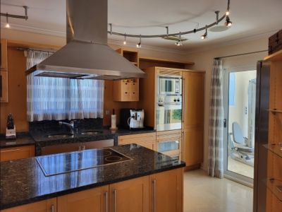 Cuisine moderne avec des armoires en bois clair, des plans de travail en granit foncé, un îlot avec plaque de cuisson intégrée et des appareils en acier inoxydable. Accès à une salle de sport.