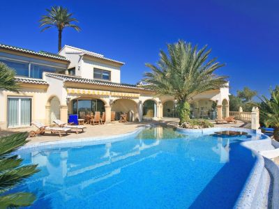 Grande piscine en mosaïque bleue avec entrée plage, îlot de palmiers et table aquatique. La villa propose une naya couverte et une salle de sport vitrée.