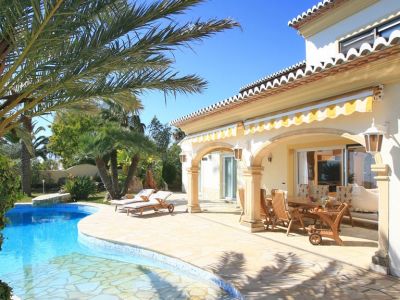 L'extérieur de la villa comprend une piscine de forme libre et une vaste terrasse dallée en pierre menant à une naya couverte avec un ensemble de salle à manger en bois sous des auvents rayés.