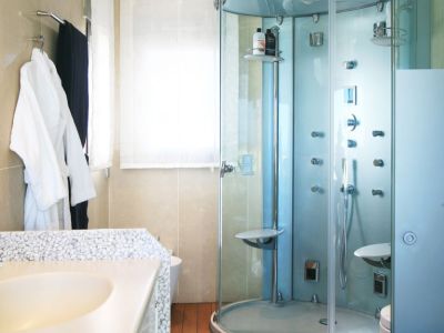 Salle de bain avec cabine de douche en verre à jets multiples, un plan de travail de lavabo texturé de galets et un sol en bois chaleureux. Lumière naturelle par la fenêtre.