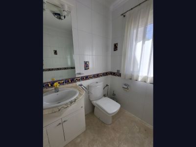 Salle de bain avec murs carrelés blancs, frise décorative et carreaux à motif coq. Elle dispose d'un lavabo sur meuble à plateau en marbre clair, de toilettes et d'une fenêtre.