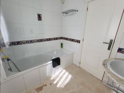 Salle de bain fonctionnelle avec baignoire blanche, pare-douche en verre et murs carrelés de blanc avec frise décorative. Dispose d'un lavabo en marbre et lumière naturelle.