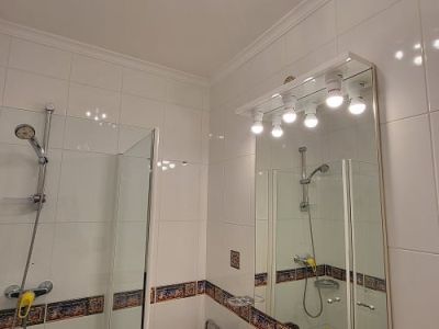 Salle de bain fonctionnelle avec carrelage blanc et frise décorative, douche vitrée et lavabo sur meuble effet marbre. Miroir éclairé et plafonnier bleu et argent.