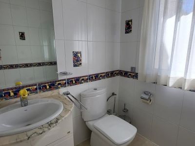 Salle de bain lumineuse avec carrelage mural blanc, frise décorative colorée et accents. Comprend une vasque sur meuble en marbre, des toilettes modernes et une fenêtre avec voilage.