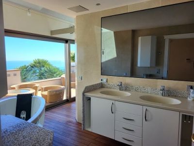 Salle de bain principale avec double vasque, baignoire balnéo et accès direct à une terrasse en bois meublée offrant une vue mer.