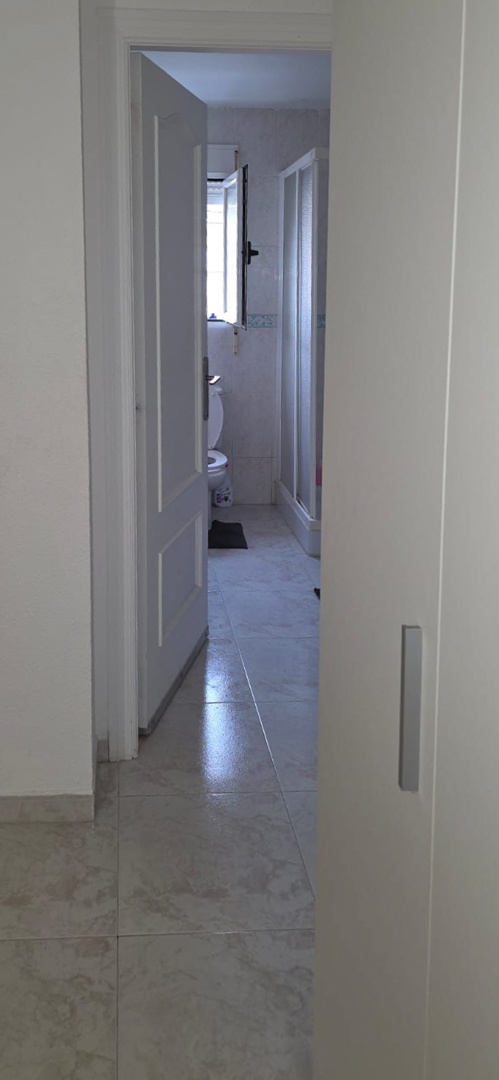 Aperçu d'une salle de bain avec carrelage au sol clair, toilettes, fenêtre et cabine de douche. Le mur est orné de carreaux avec une frise décorative.