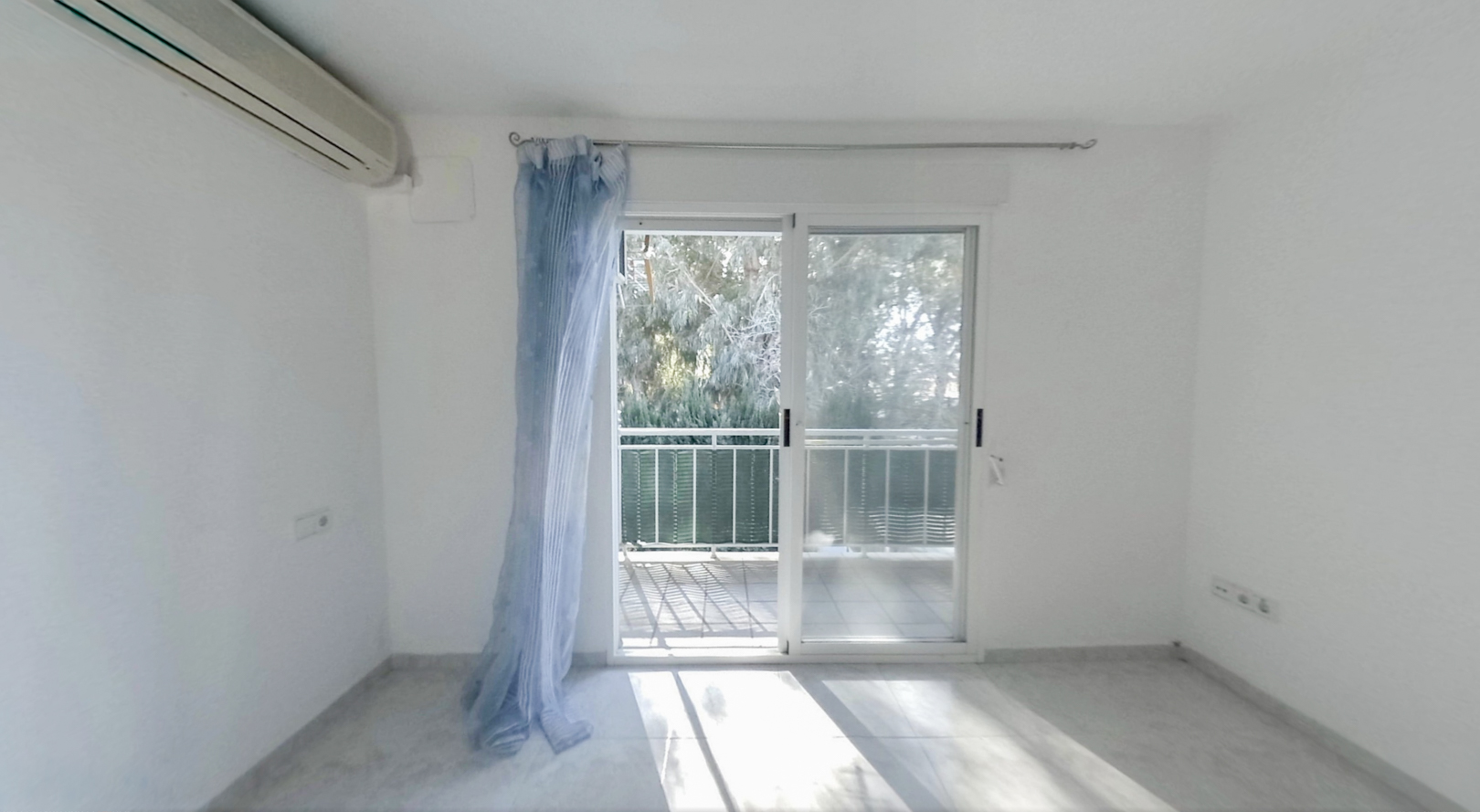 Chambre lumineuse avec climatisation et accès direct à une terrasse privée. Sol carrelé clair et vue sur la verdure extérieure.