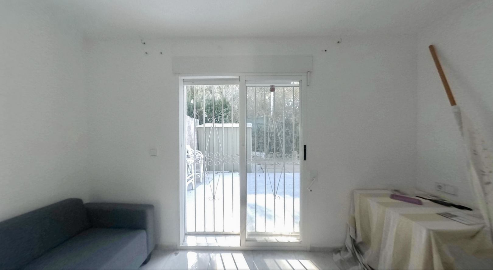 Pièce spacieuse avec portes coulissantes vitrées et barreaux de sécurité, offrant un accès direct au jardin privé, baignée de lumière naturelle sur le sol clair.