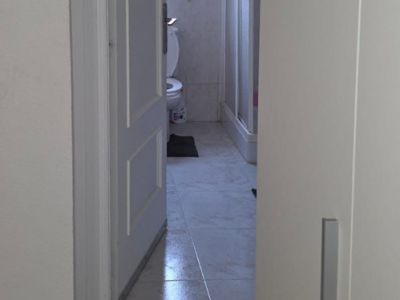 Aperçu d'une salle de bain avec carrelage au sol clair, toilettes, fenêtre et cabine de douche. Le mur est orné de carreaux avec une frise décorative.