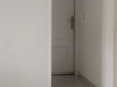 Couloir intérieur avec carrelage clair et murs blancs texturés, menant à une porte à panneaux, agrémenté d'un petit ornement mural.
