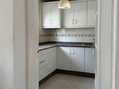 Cuisine fonctionnelle avec des armoires blanches, un plan de travail en granit moucheté et un dosseret carrelé. Une suspension éclaire la pièce, offrant un potentiel de modernisation.