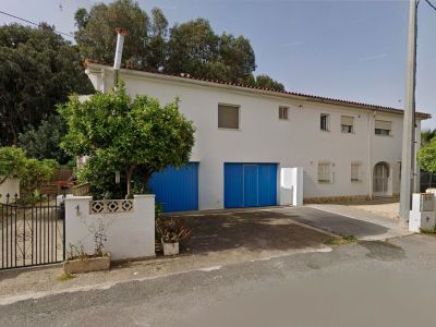 Façade avant de la villa jumelée, présentant une façade blanche, deux grandes portes de garage bleues et un oranger près du portail en fer forgé.