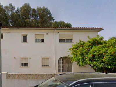 La façade blanche de la villa à deux étages présente un toit de tuiles, une entrée arquée et des fenêtres sécurisées. Un oranger mature, chargé de fruits, se dresse au premier plan.