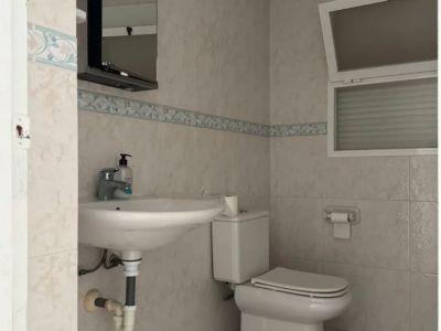 Salle de bain fonctionnelle avec carrelage clair, frise décorative et fenêtre oscillo-battante. Comprend un lavabo suspendu, des toilettes et un miroir avec éclairage intégré.