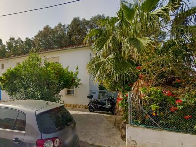 Vue extérieure de l'entrée pavée de la villa, avec un oranger chargé de fruits, un palmier et une végétation méditerranéenne luxuriante.