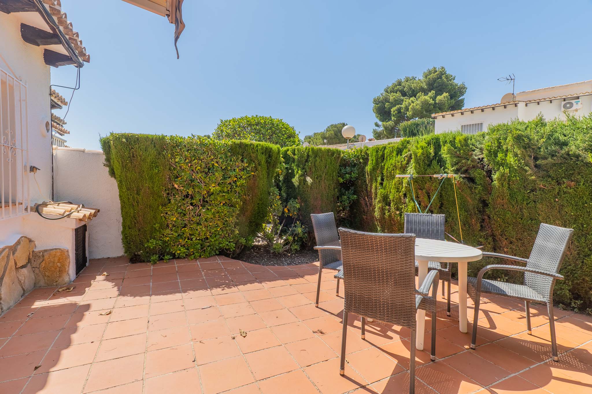 Terrasse arrière privée et ensoleillée avec carrelage en terre cuite, mobilier de jardin et une haie haute offrant une intimité totale.