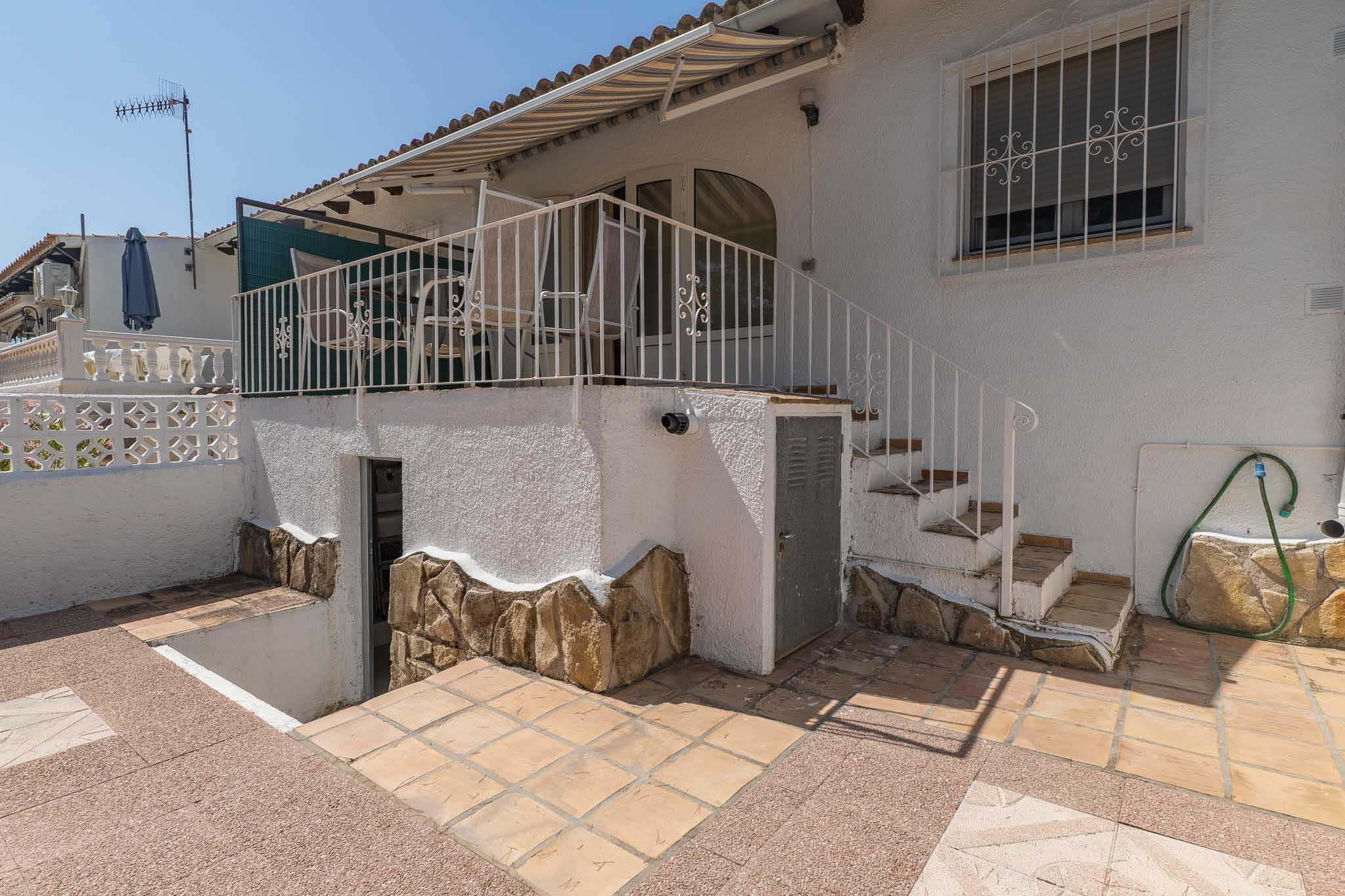 Terrasse d'angle avec carrelage clair, aménagée d'un canapé et d'une table basse d'extérieur. Offre des vues dégagées et de l'ombre sous un store blanc, invitant à la détente.