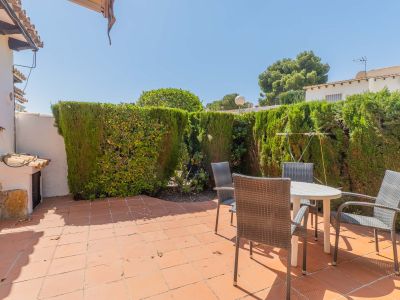 Terrasse arrière privée et ensoleillée avec carrelage en terre cuite, mobilier de jardin et une haie haute offrant une intimité totale.