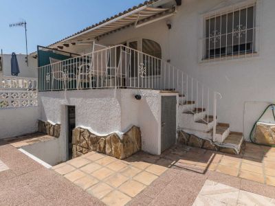Terrasse d'angle avec carrelage clair, aménagée d'un canapé et d'une table basse d'extérieur. Offre des vues dégagées et de l'ombre sous un store blanc, invitant à la détente.