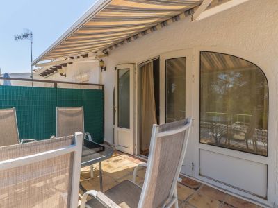 Terrasse extérieure ensoleillée avec carrelage en terre cuite, store rayé et mobilier de jardin. Accès direct à l'intérieur par portes doubles et fenêtre arquée.