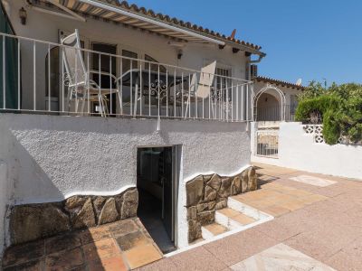 Terrasse surélevée avec balustrade en fer forgé et auvent, donnant sur un patio inférieur carrelé avec accès à l'espace de rangement. Murs avec soubassement en pierre décorative.
