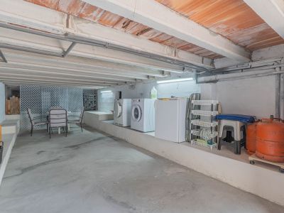 Vaste espace inférieur avec buanderie équipée, rangements et coin salon informel. Le plafond présente des poutres en béton et des briques apparentes.