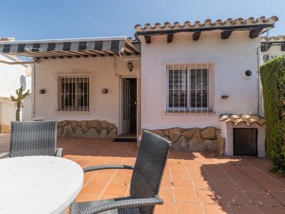 Vaste terrasse extérieure avec carrelage en terre cuite, mobilier de repas et store rayé rétractable. Façade blanche avec soubassement en pierre, grilles de sécurité et tuiles traditionnelles.