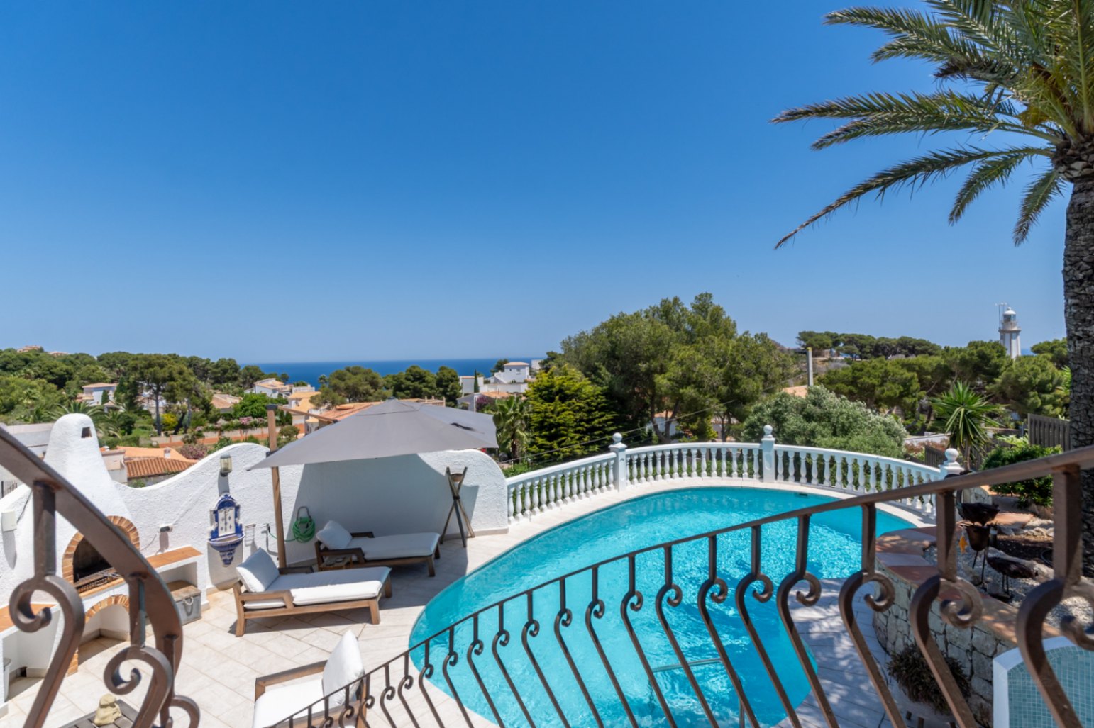 Piscine incurvée avec terrasse carrelée, barbecue extérieur traditionnel et vues panoramiques sur la Méditerranée et le phare.