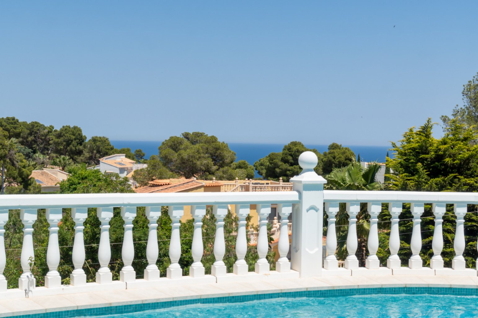 Une balustrade blanche classique encadre les vues panoramiques sur la mer Méditerranée depuis la piscine, surplombant les toits de Jávea et la verdure.