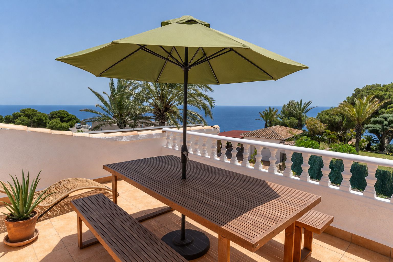 Vaste terrasse sur le toit avec table et bancs en bois, parasol vert et vues panoramiques sur la mer Méditerranée, encadrées par une balustrade blanche.