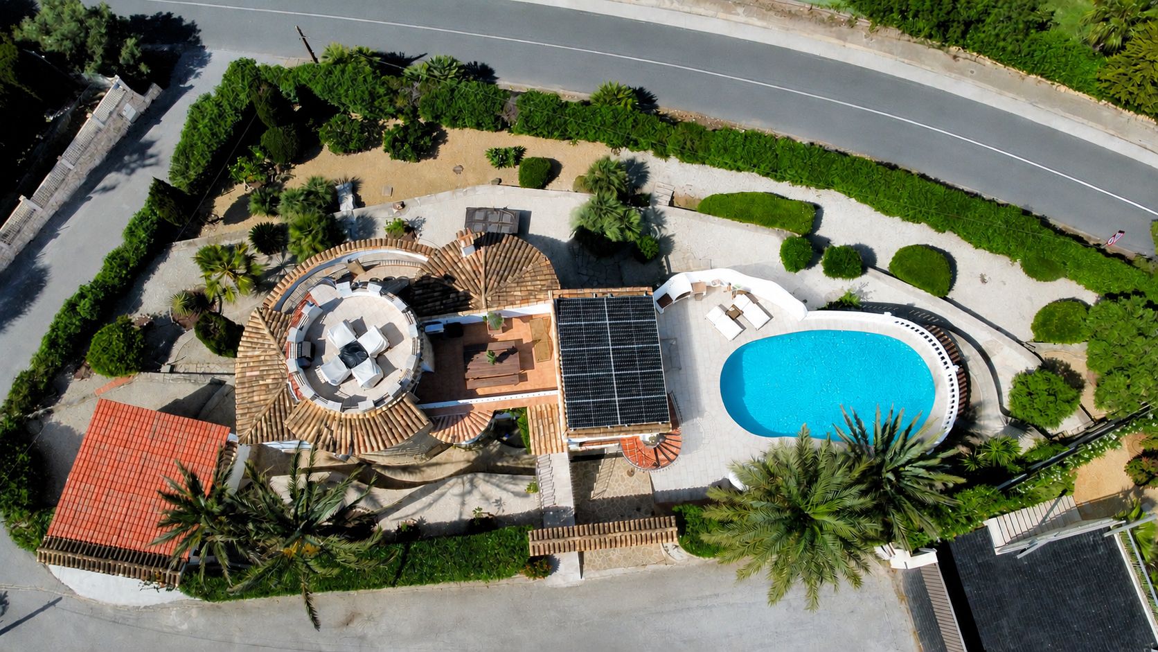 Vue aérienne de la villa, présentant la piscine ovale, les panneaux solaires et la terrasse circulaire sur le toit avec mobilier extérieur.