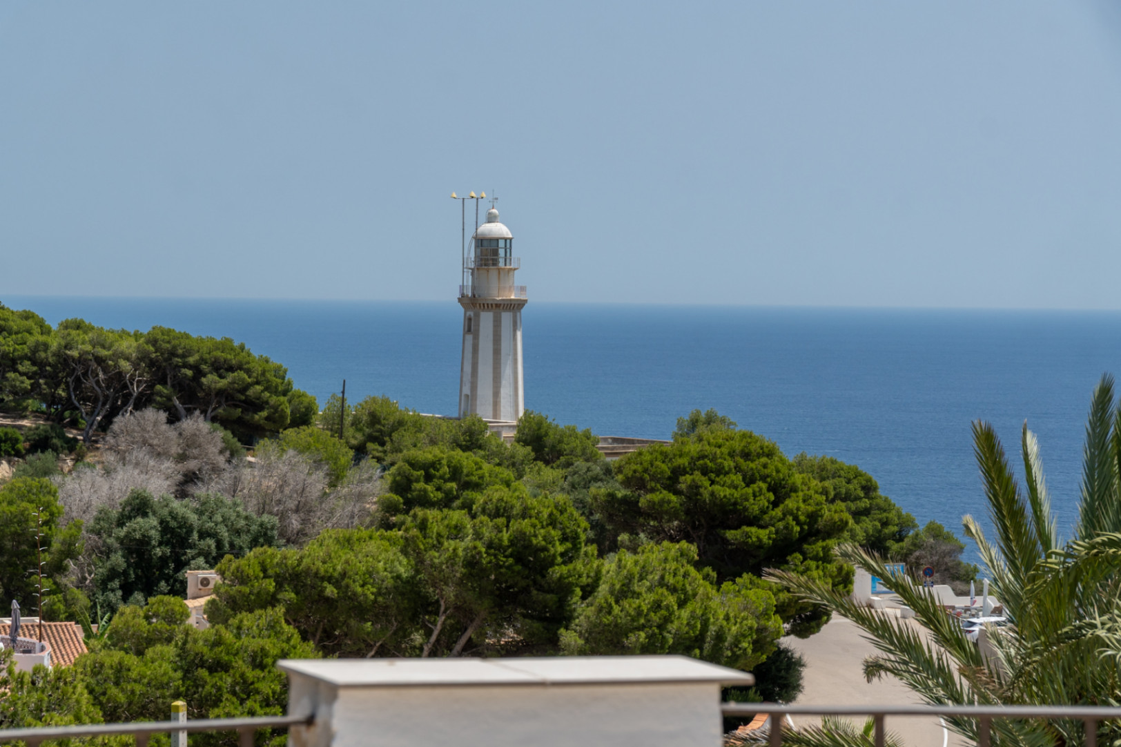 Vue du phare blanc rayé de gris, dressé sur une colline verdoyante, avec la vaste mer Méditerranée bleue s'étendant à l'horizon sous un ciel clair.