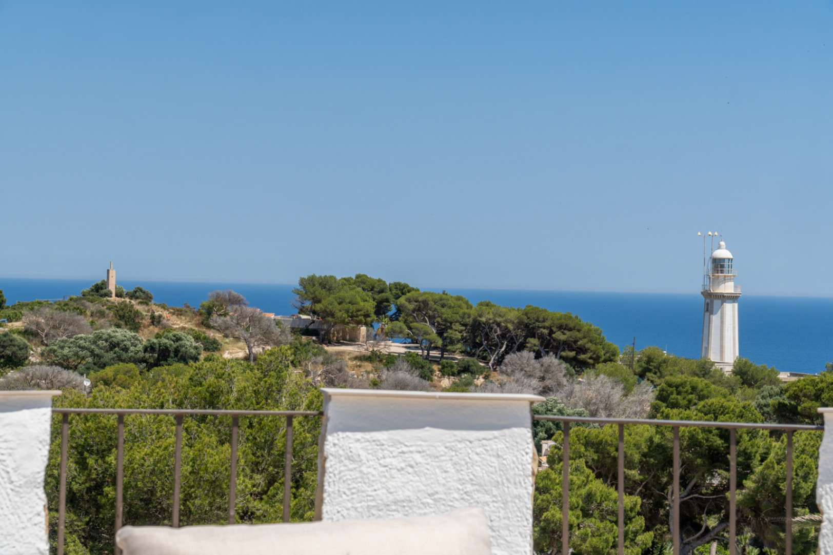 Vue panoramique depuis la terrasse avec balustrade métallique, présentant la mer Méditerranée, un phare et une tour de pierre au loin.