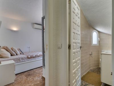 Aperçu d'une chambre avec sol effet marbre et climatisation, faisant face à une salle de bain aux murs carrelés beige, fenêtre arquée et sol en mosaïque avec meuble vasque.