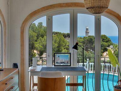 Bureau lumineux avec une fenêtre arquée offrant une vue panoramique sur la mer, le phare et la piscine.
