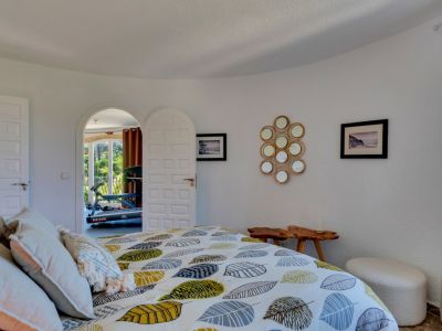 Chambre à coucher avec murs blancs texturés, lit design à motif de feuilles et porte cintrée ouvrant sur une pièce lumineuse avec équipement de sport.