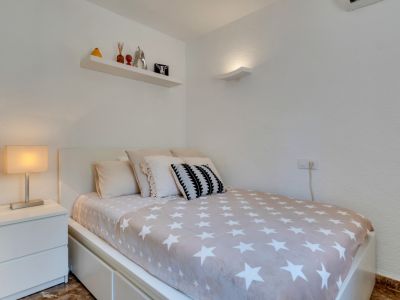 Chambre individuelle avec lit moderne, couette étoilée, table de chevet blanche et étagère murale décorée. Éclairage mural discret et climatisation.