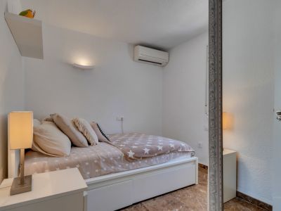 Chambre secondaire avec murs blancs texturés, un lit avec une couette à motif d'étoiles et une lampe de chevet moderne. Comprend une unité de climatisation et un sol carrelé.