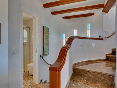 Escalier courbe en marbre brun avec rampe en bois, poutres apparentes et fenêtres à vitraux colorés. Accès à une salle de bain avec douche.