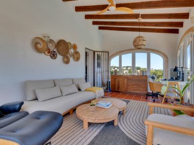 Lumineuse terrasse vitrée avec poutres en bois apparentes, carrelage en terre cuite et fenêtres cintrées offrant des vues sur le paysage. Intègre un coin salon et un bureau.