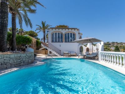 Piscine incurvée d'eau bleue avec espace solarium, barbecue extérieur et villa méditerranéenne blanche, entourée de palmiers et de verdure luxuriante.