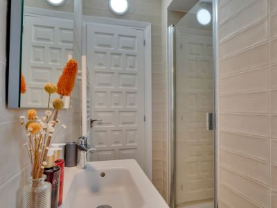 Salle de bain compacte avec lavabo blanc, robinetterie chromée et douche vitrée. Les murs sont carrelés de beige, porte à panneaux blancs.