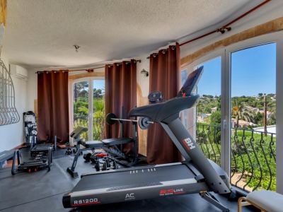 Salle de sport à domicile équipée d'un tapis de course et d'haltères, offrant des vues panoramiques sur la verdure et le paysage depuis ses grandes fenêtres.