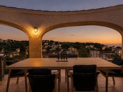 Terrasse élégante avec arches au crépuscule, dotée d'une table à manger en bois. Profitez des vues panoramiques sur la zone résidentielle illuminée et l'horizon marin.