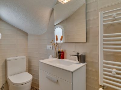 Toilettes fonctionnelles avec murs carrelés clairs, meuble-lavabo blanc et WC. Un miroir reflète une fenêtre arquée et un sèche-serviettes.