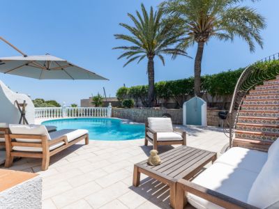 Vaste terrasse de piscine avec chaises longues en bois, un salon de jardin et un escalier courbé aux contremarches carrelées. Des palmiers et une douche extérieure agrémentent l'espace.
