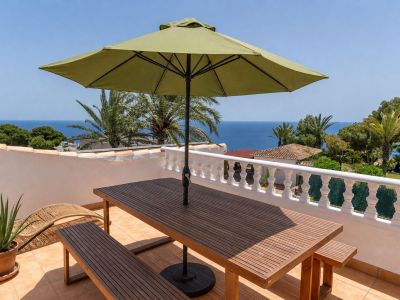 Vaste terrasse sur le toit avec table et bancs en bois, parasol vert et vues panoramiques sur la mer Méditerranée, encadrées par une balustrade blanche.