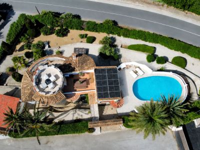 Vue aérienne de la villa, présentant la piscine ovale, les panneaux solaires et la terrasse circulaire sur le toit avec mobilier extérieur.